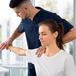 Physiotherapist helping a woman with shoulder rehabilitation exercises during therapy session